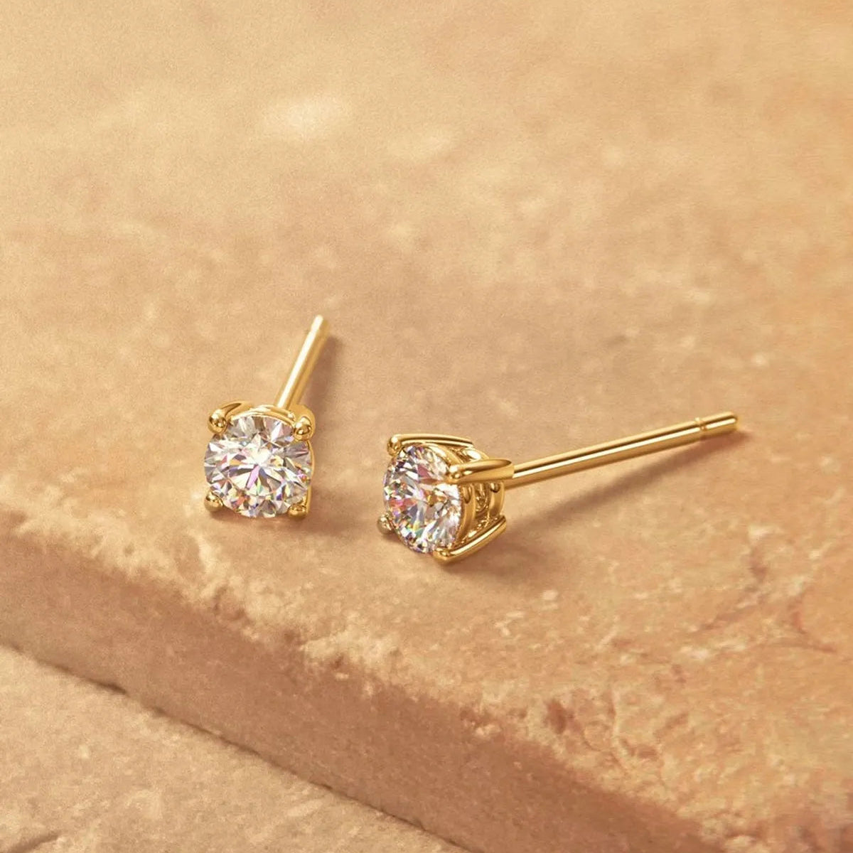 Gold stud earrings with clear gemstones on a beige surface