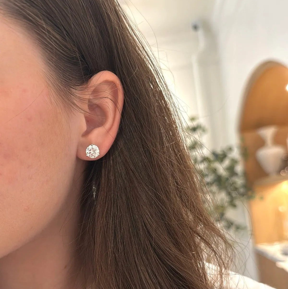 Close-up of a person wearing diamond earrings with a blurred indoor background