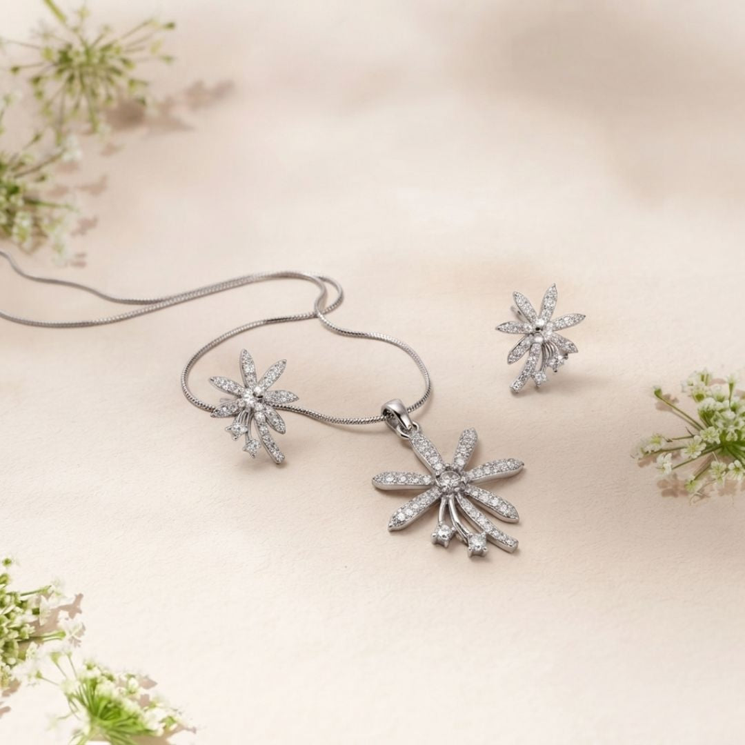 Diamond flower pendant necklace and matching stud earrings on a beige fabric background with white flowers