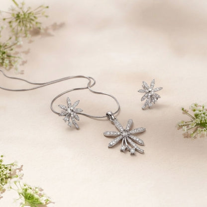 Diamond flower pendant necklace and matching stud earrings on a beige fabric background with white flowers