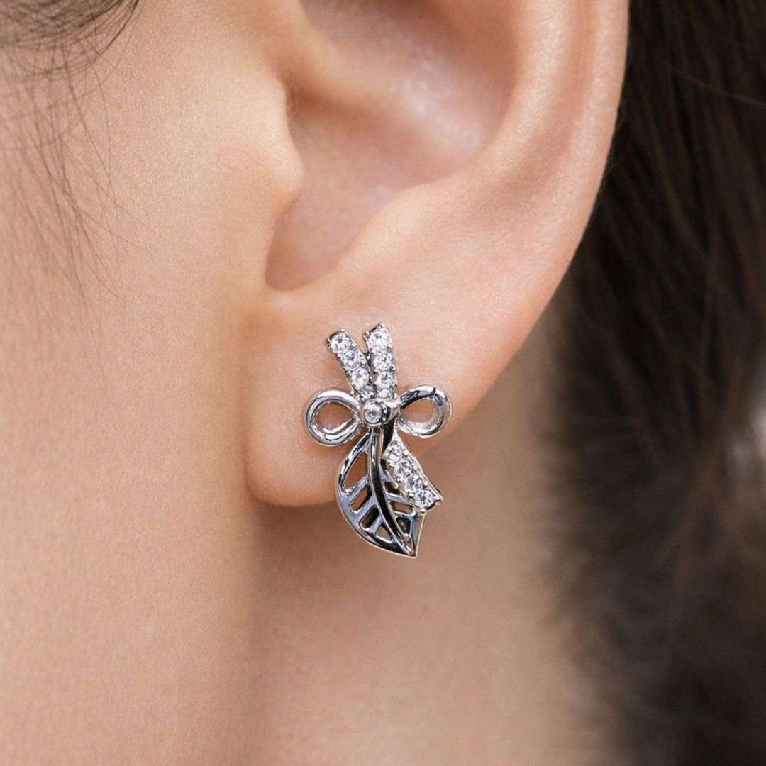 Silver bow-shaped earring worn on an ear with a blurred background