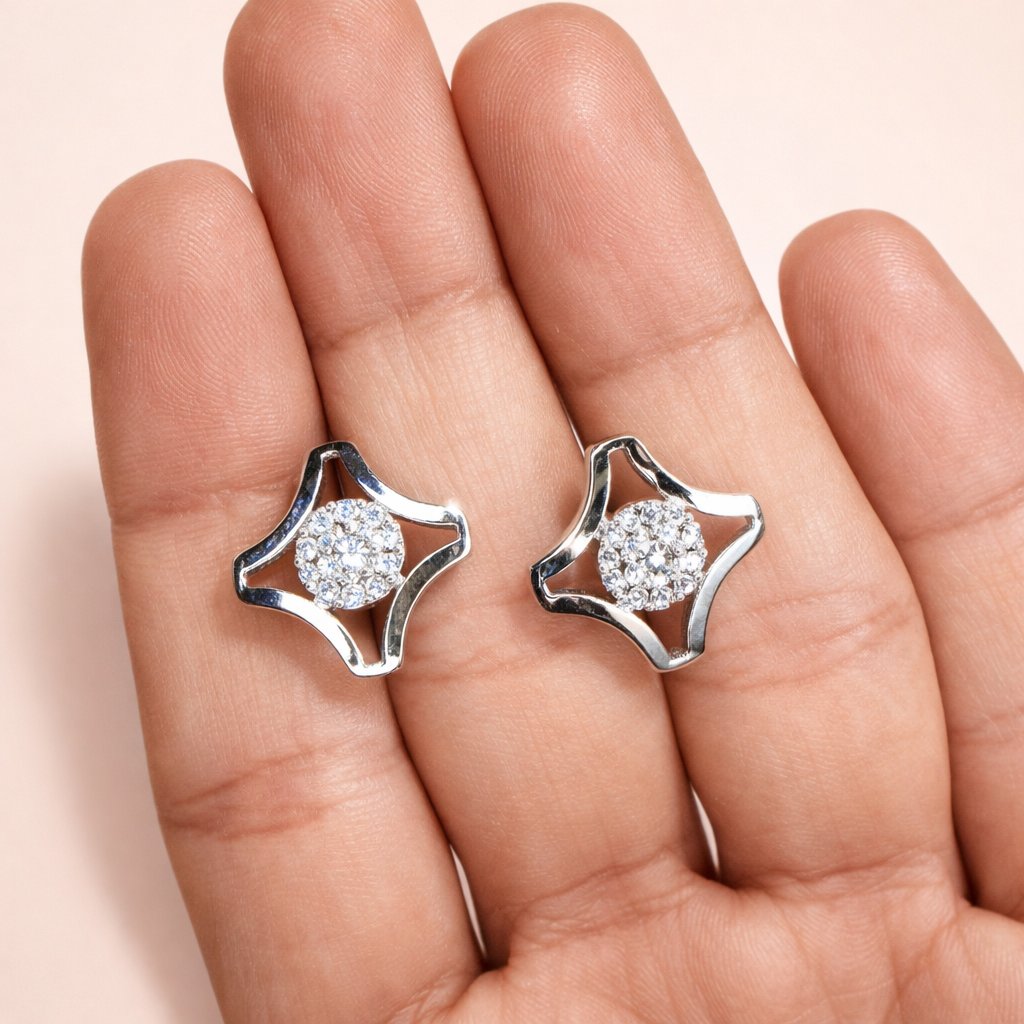 Silver AD Earrings for Women with clear stones held between fingers on a light pink background