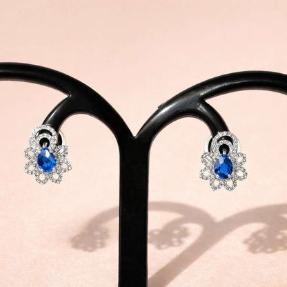 Pair of silver AD Earrings for Women with blue gemstones on a light pink background