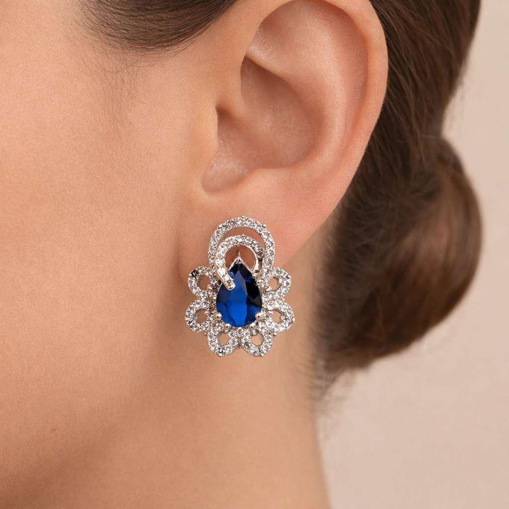 Close-up of an ear wearing a decorative AD Earrings for Women with a blue gemstone on a neutral background
