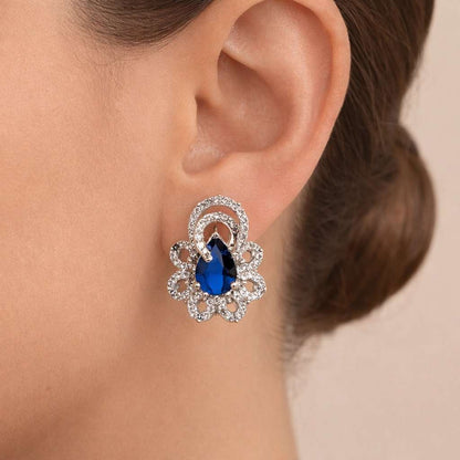 Close-up of an ear wearing a decorative AD Earrings for Women with a blue gemstone on a neutral background