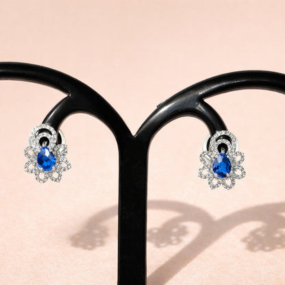 Pair of silver AD Earrings for Women with blue gemstones on a light pink background