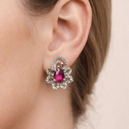Close-up of an ear wearing a decorative earring with a red gemstone on a neutral background