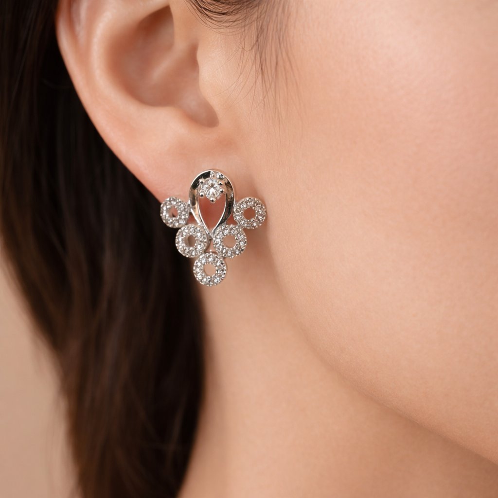 Close-up of a silver AD Earrings for Women with clear stones on an ear against a neutral background