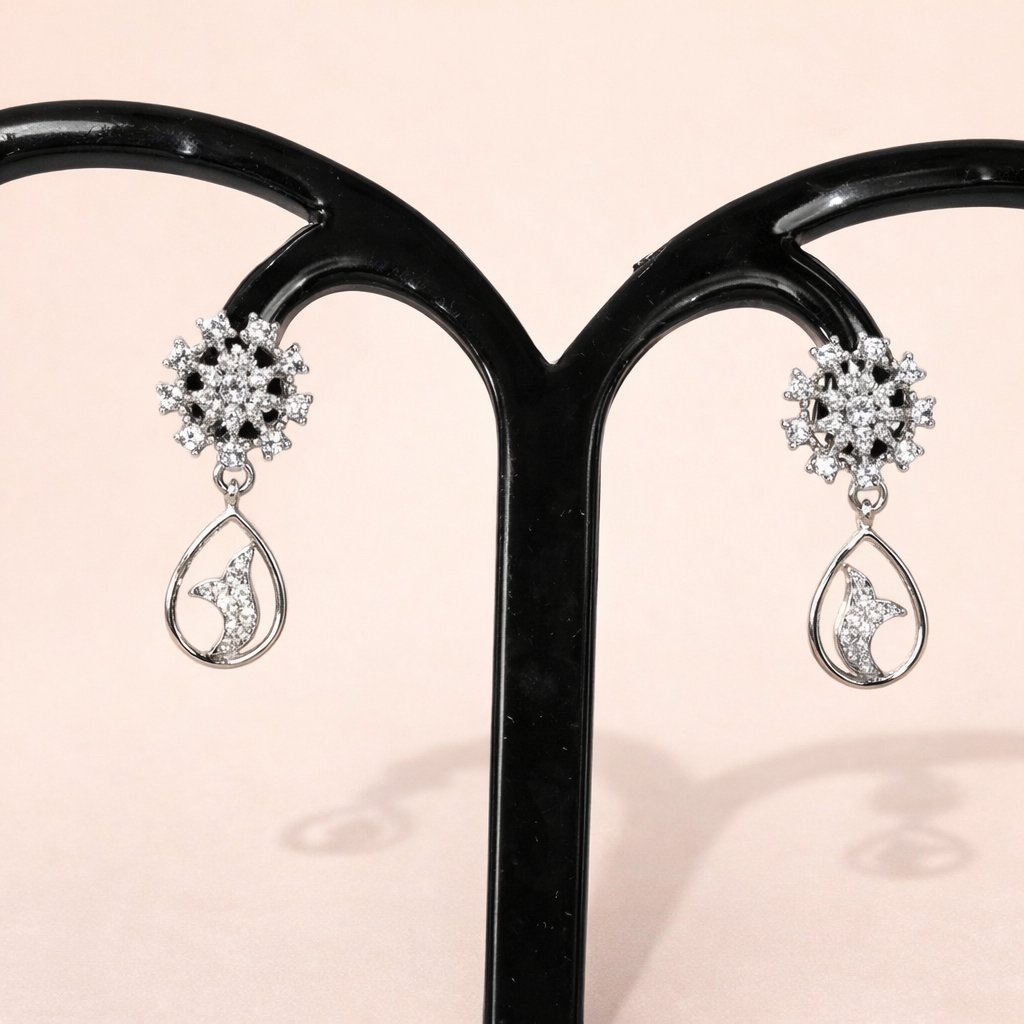 Pair of silver AD Earrings for Women with teardrop design on a black stand against a pink background