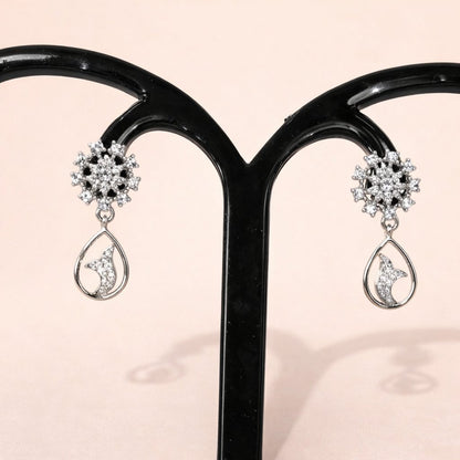 Pair of silver AD Earrings for Women with teardrop design on a black stand against a pink background