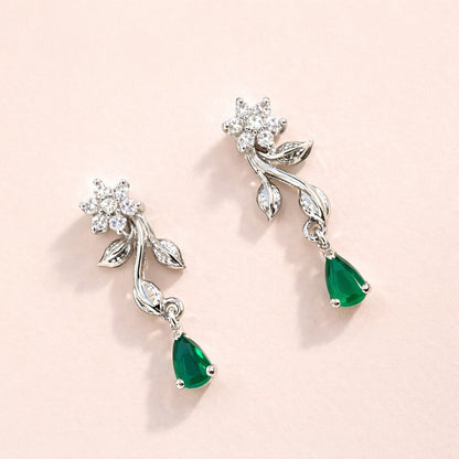 Pair of AD Earrings for Women with emerald drops on a light pink background
