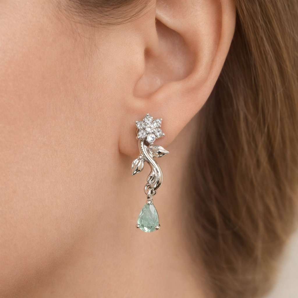 Close-up of a silver AD Earrings for Women with a green gemstone worn by a person.