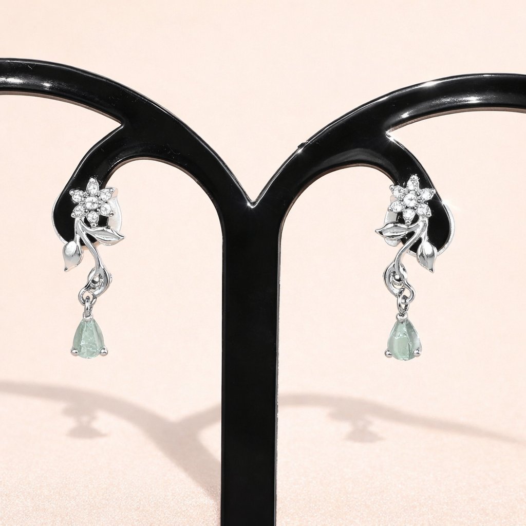 Pair of AD Earrings for Women with floral design and green gemstones on a black stand.