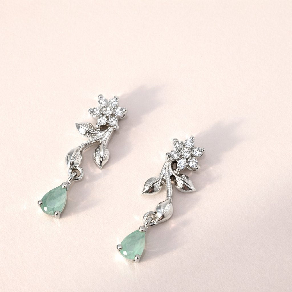 Pair of silver AD Earrings for Women with green gemstones on a light pink background