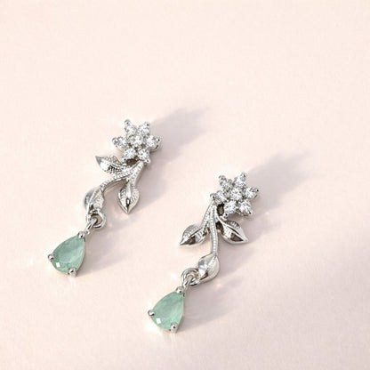 Pair of silver AD Earrings for Women with green gemstones on a light pink background