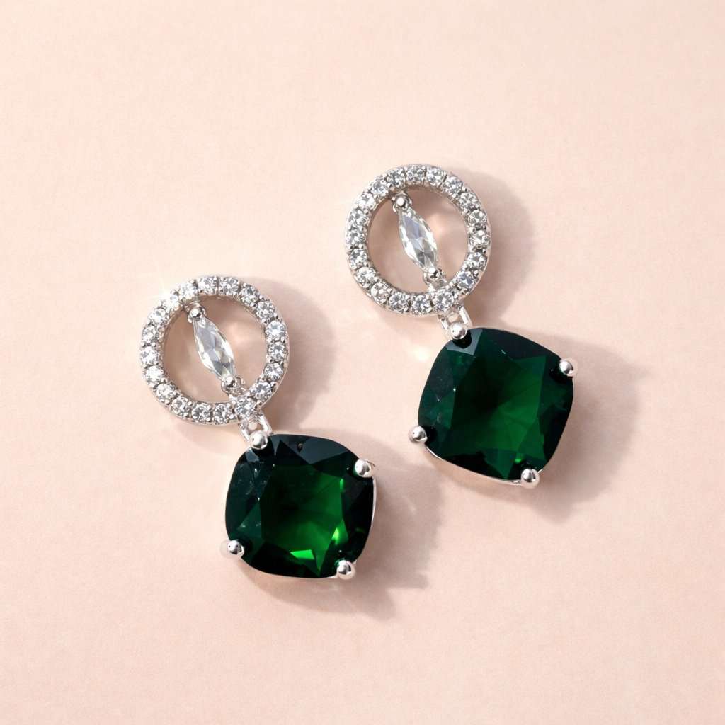 Pair of AD Earrings for Women with green gemstones and silver loops on a beige background