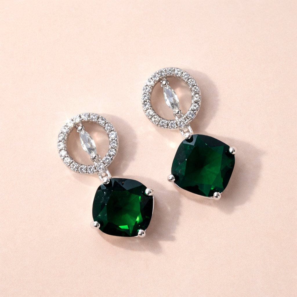 Pair of AD Earrings for Women with green gemstones and silver loops on a beige background