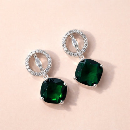 Pair of AD Earrings for Women with green gemstones and silver loops on a beige background