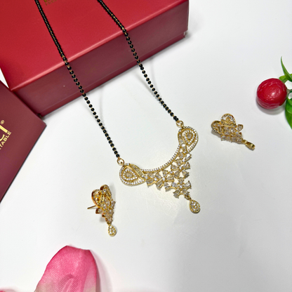 Gold AD Mangalsutra and earrings on a white surface with a red box and pink flower.