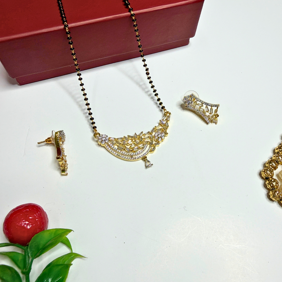 Gold necklace and earrings with a red box on a white surface.