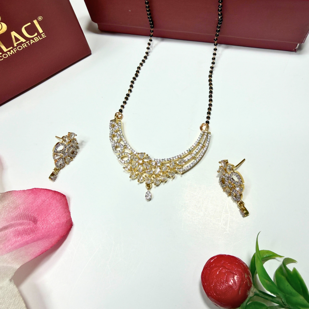 Gold AD Mangalsutra and earrings on a white surface with a pink flower and red fruit.