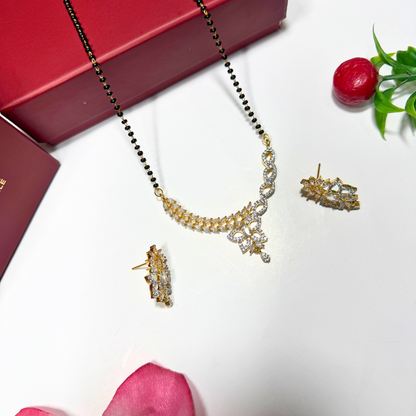 Gold AD Mangalsutra and earrings on a white surface with a red box and pink petals.