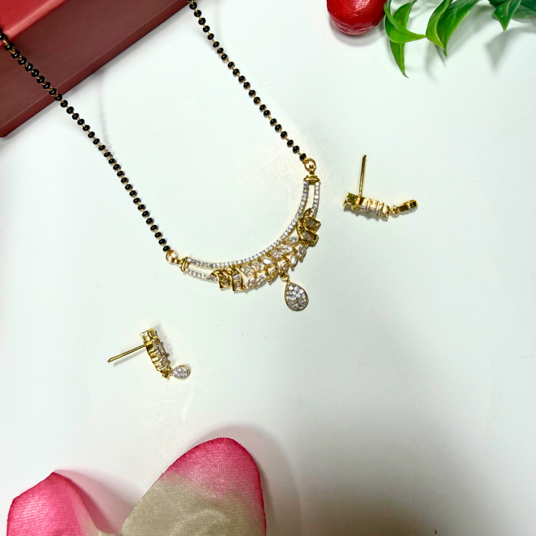 Gold AD Mangalsutra and earrings on a white surface with pink petals and green leaves.