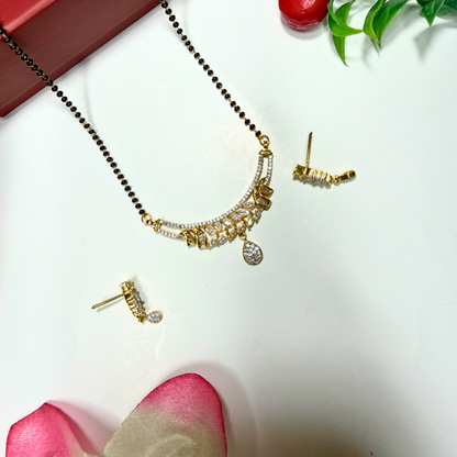 Gold AD Mangalsutra and earrings on a white surface with pink petals and green leaves.