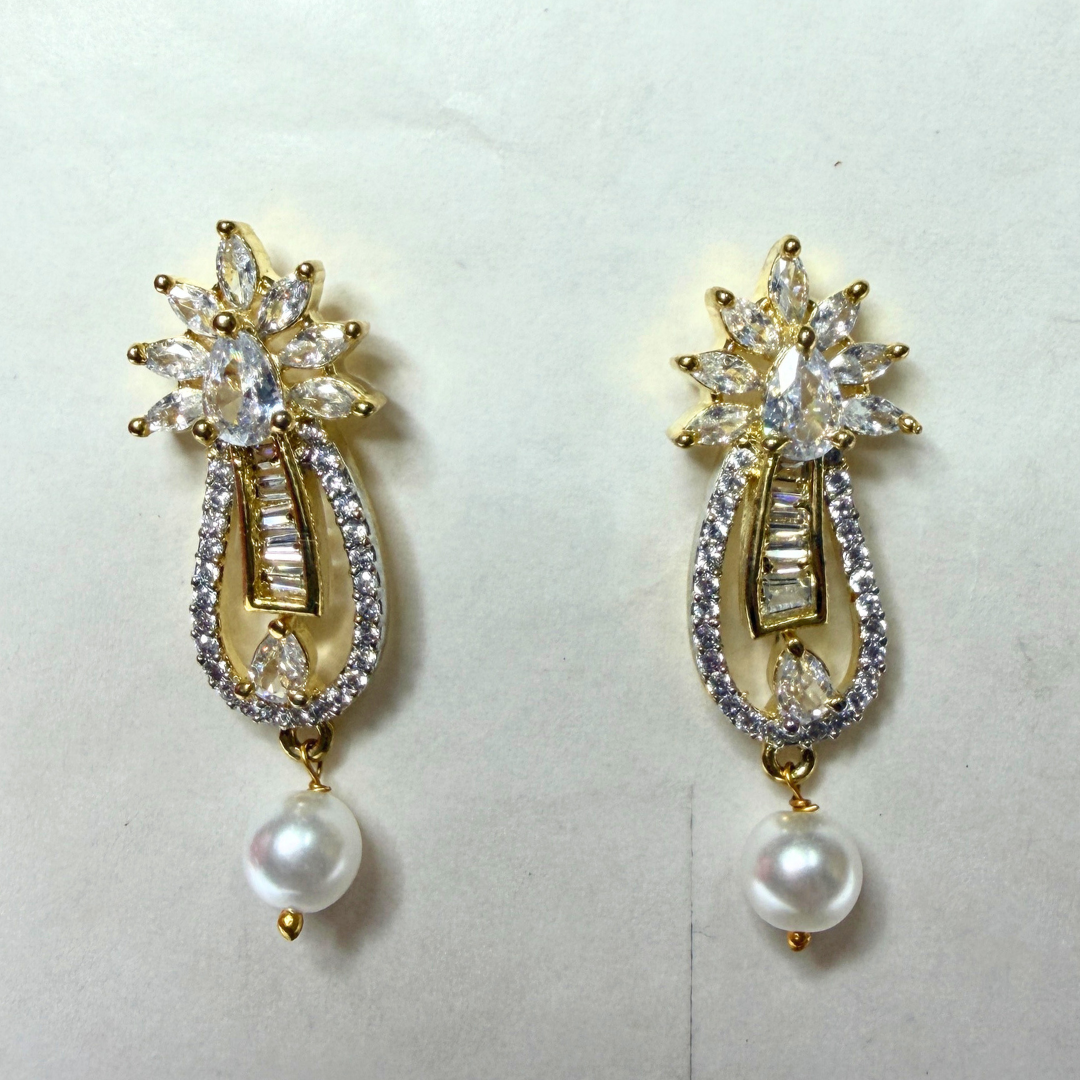 Pair of gold AD earrings with clear gemstones and pearl drops on a light gray background