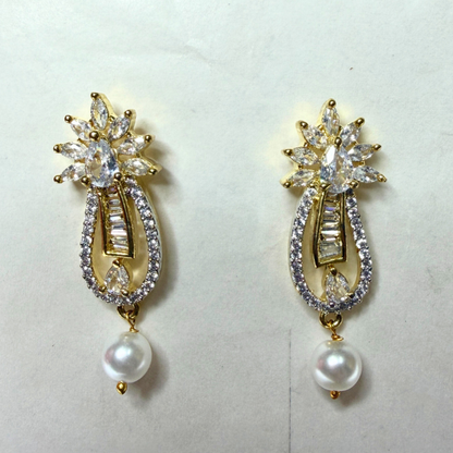 Pair of gold AD earrings with clear gemstones and pearl drops on a light gray background
