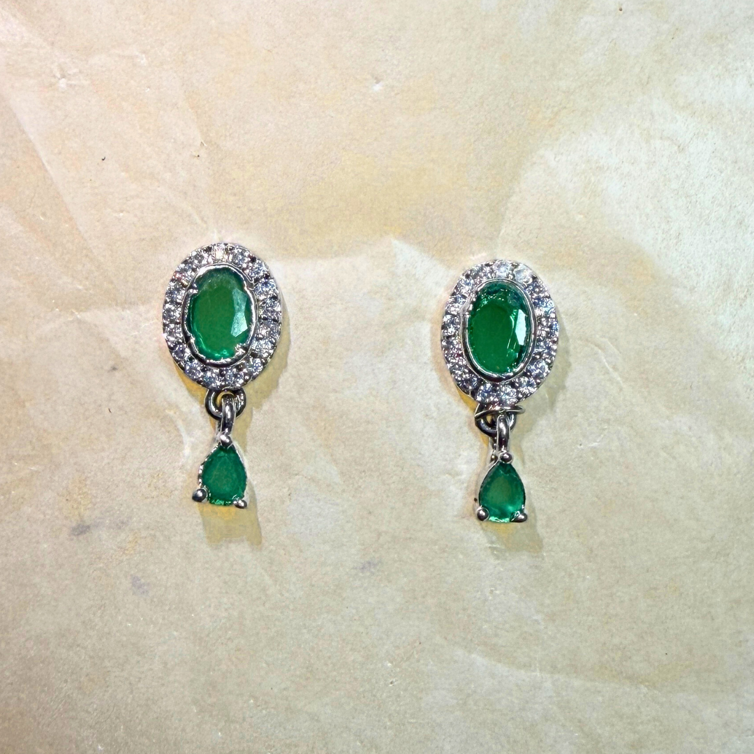 Pair of emerald green earrings with silver accents on a beige stone background