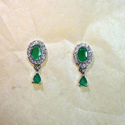 Pair of emerald green earrings with silver accents on a beige stone background