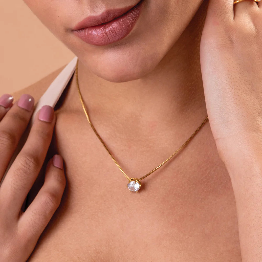 Close-up of a person wearing a gold necklace with a diamond pendant on a beige background