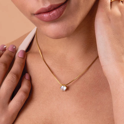 Close-up of a person wearing a gold necklace with a diamond pendant on a beige background
