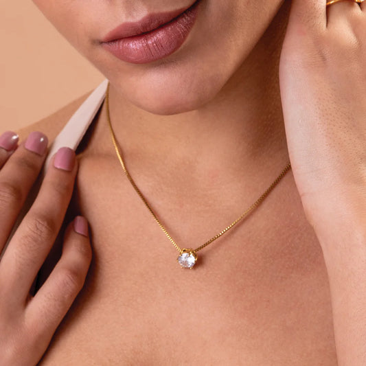 Close-up of a person wearing a gold necklace with a diamond pendant on a beige background