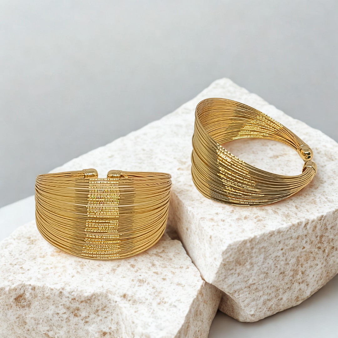 Two gold plated bracelets on a textured stone surface with a light gray background