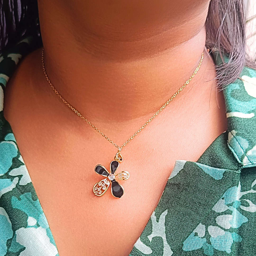 Necklace with a black and gold pendant worn by a person in a floral shirt.