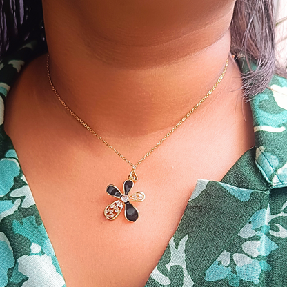 Necklace with a black and gold pendant worn by a person in a floral shirt.